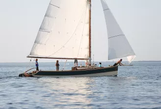Voilier traditionnel aux voiles blanches naviguant avec des passagers sur les eaux calmes près d'Arcachon, avec des membres d'équipage visibles sur le pont