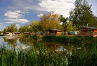 Cabanes et maisons écologiques en bois se reflétant dans l'eau calme, entourées de roseaux et d'arbres en automne dans un village durable au bord du lac près de Bordeaux.
