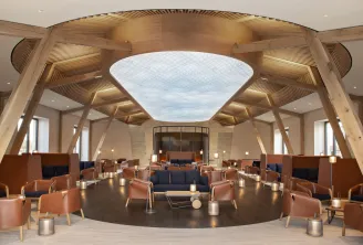 Salon moderne de luxe avec structures architecturales en bois, grande verrière zénithale, fauteuils en cuir cognac, sol sombre et mobilier contemporain conçu pour événements professionnels.
