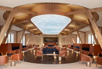 Salon de luxe moderne avec architecture en bois, chaises en cuir cognac disposées autour d'un sol central sombre, grande verrière et scène au Château de Ferrand à Bordeaux.