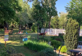 Vaste espace vert avec arbres matures, chaises colorées, clôture blanche, haies taillées et panneaux de signalisation dans les jardins écologiques du Novotel Bordeaux Mérignac.