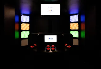Salle de jeu immersive avec panneaux illuminés multicolores, deux écrans affichant 'Bienvenue!' et l'interface 'Quiz', et des boutons de contrôle rouges sur un sol sombre au Mercure Bordeaux Centre.