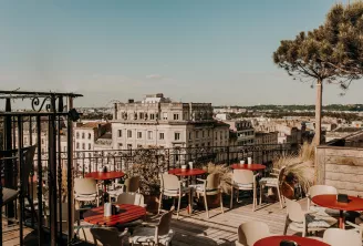 Terrasse sur le toit de l'hôtel Intercontinental Bordeaux avec parasols rouges et chaises beiges offrant une vue panoramique sur l'architecture historique et le paysage urbain de Bordeaux