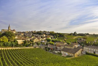 Vue aérienne du village de Saint-Émilion avec son clocher dominant les vignobles en terrasses de la région bordelaise, entouré de maisons en pierre traditionnelles et de collines verdoyantes.