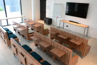 Salle de réunion ou de formation moderne avec des unités de mobilier modulable en bois sur roulettes, coussins bleu-vert, écran TV mural, tableau blanc et grandes fenêtres donnant sur l'horizon urbain de Bordeaux.