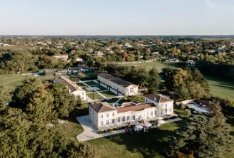 Vue aérienne du Château Gassies, un élégant domaine néoclassique blanc aux espaces aménagés, entouré de verdure et de paysage rural près de Bordeaux, France.