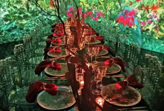 Une expérience gastronomique immersive au Cube aux Bassins des Lumières à Bordeaux, avec une table élégante dressée de couverts, fleurs rouges et verres, entourée d'une projection numérique représentant un jardin fleuri luxuriant.