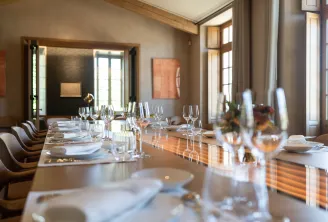 Salle à manger élégante avec une longue table en bois dressée pour un banquet professionnel, verres fins, couverts et décoration contemporaine avec grandes fenêtres et œuvres d'art moderne.
