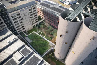 Vue aérienne du paysage urbain de Bordeaux montrant des immeubles résidentiels modernes, des cours verdoyantes, des panneaux solaires sur les toits et des structures cylindriques distinctives en béton avec des personnes qui y grimpent
