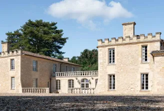 Château de Ferrand, demeure en pierre aux tours crénelées et grandes fenêtres, entouré d'une cour en gravier sous un ciel bleu dégagé près de Saint-Émilion à Bordeaux.