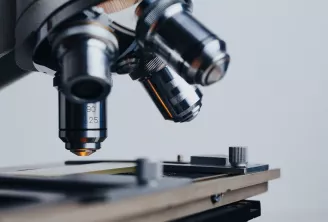 Microscope avec plusieurs objectifs montés sur une platine, mettant en évidence un objectif de grossissement 90x25 sur un fond flou d'équipements de laboratoire.