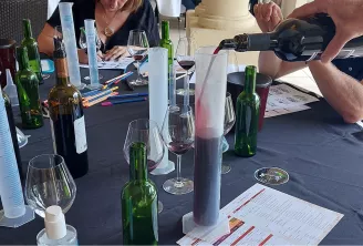 Atelier de dégustation de vin en team building à Bordeaux où les participants sont réunis autour d'une table avec des bouteilles, des verres, des fiches de dégustation, et une personne versant du vin lors d'une activité de création vinicole éco-responsabl