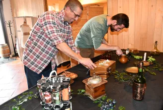 Deux hommes participent à une activité de team building dans une salle rustique en bois, examinant et manipulant des objets sur une table noire décorée de plantes et d'accessoires vintage.