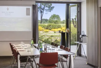 Salle de conférence contemporaine du Golf du Médoc Resort MGallery avec baies vitrées panoramiques donnant sur des jardins paysagés, des arbustes aux fleurs jaunes et le paysage campagnard environnant, équipée de chaises bordeaux autour d'une table de réu