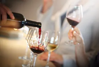 Du vin rouge versé d'une bouteille dans un verre lors d'une dégustation de vin, avec en arrière-plan d'autres participants tenant des verres de vin.