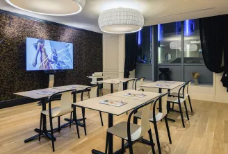 Salle de conférence moderne de l'hôtel Mercure Bordeaux Gare Atlantic avec tables blanches, chaises noires, grand écran d'affichage avec contenu animé, mur d'accent texturé foncé, luminaires plafond contemporains et parois vitrées avec éclairage accentué 