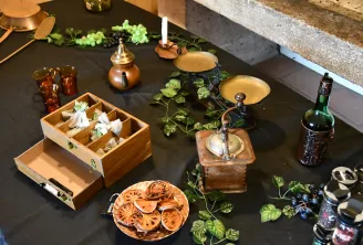 Mise en place élégante avec tranches d'agrumes séchés, boîtes en bois contenant des serviettes blanches, chandeliers en laiton, guirlande de houblon frais, bouteille de vin et instruments en laiton sur surface noire, évoquant la culture viticole bordelais
