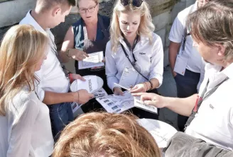 Un groupe de jeunes personnes réunies en plein air consultant des documents et des cartes lors du Rallye Pédestre des Ateliers de Bacchus à Bordeaux, avec une animatrice au centre.