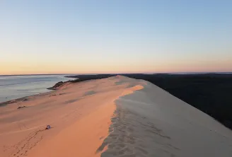 Vue aérienne de la Dune du Pilat au coucher de soleil avec les dunes de sable doré, la forêt de pins et les eaux calmes du Bassin d'Arcachon