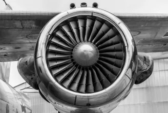 Gros plan d'un turboréacteur double flux montré sur l'aile d'un avion, mettant en évidence les aubes du ventilateur et le carter métallique en photographie noir et blanc.