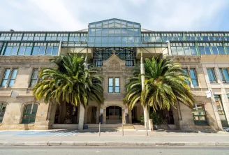 Bâtiment historique en pierre d'architecture néoclassique avec extension de toit en verre moderne, deux grands palmiers encadrant l'entrée et portes en arc à Bordeaux.