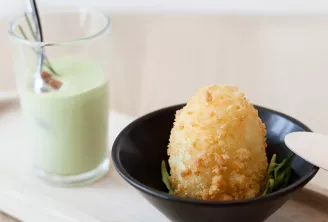 Assiette gastronomique présentant un dôme de pâtisserie dorée sur une assiette noire garnie de romarin, accompagnée d'une boisson vert pâle dans un verre
