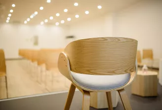 Chaise en bois moderne avec assise rembourrée blanche dans un espace intérieur minimaliste et lumineux, éclairage encastré au plafond et mobilier flou en arrière-plan
