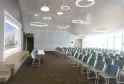 Salle de conférence moderne du Hilton Garden Inn Bordeaux Centre avec rangées de chaises vertes, luminaires suspendus circulaires, murs blancs et grand écran d'affichage présentant un projet architectural