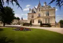 Château Pape Clément à Bordeaux, imposante demeure en pierre du XIXe siècle avec toit mansardé et tourelles, entourée de jardins aménagés et parterres de fleurs rouges