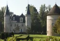 Château d'Agassac près de Bordeaux, présentant un château en pierre blanche avec deux tours élancées aux toits pointus noirs, un toit mansardé central et une tour ronde séparée à droite, entouré de jardins aménagés avec pelouse verte et topiaires.