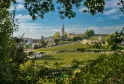 Vue panoramique d'une ville médiévale avec un clocher d'église et des fortifications en pierre dominant des vignobles en terrasses sous un ciel bleu nuageux.
