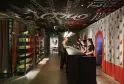 Espace d'accueil moderne de l'hôtel Mama Shelter à Bordeaux avec design contemporain, comptoir noir, personnel accueillant les clients, vitrines éclairées en vert, éléments architecturaux rouges, papier peint motifs et plafond graphique.