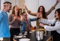 Un groupe de cinq personnes profitant d'une dégustation de vin autour d'une table avec des verres de vin et des assiettes, riant et célébrant ensemble dans une salle intérieure.