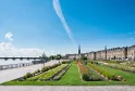 Promenade riveraine à Bordeaux avec espaces verts aménagés, jardins ornementaux et bâtiments historiques en pierre bordant la Garonne sous un ciel bleu dégagé.